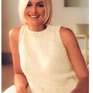 May include: A white sleeveless knitted top with a high neckline. The top is made of a soft, textured yarn.