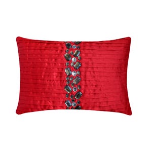 May include: A rectangular red throw pillow featuring horizontal pleats across the entire surface. A vertical band runs down the center, embellished with a dense arrangement of dark gray and clear faceted crystals of varying shapes and sizes.