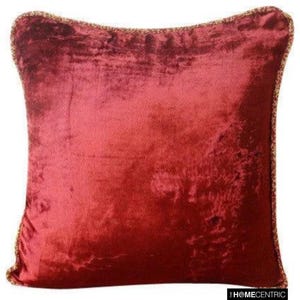 Pode incluir: Uma almofada de veludo vermelho escuro com uma borda dourada.