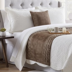 Puede incluir: Una colcha acolchada blanca con borde festoneado, que incluye un camino de cama de terciopelo marrón y un cojín cuadrado a juego. Una bandeja de madera sostiene una taza de cerámica blanca y una vela de pilar blanca sobre la cama.