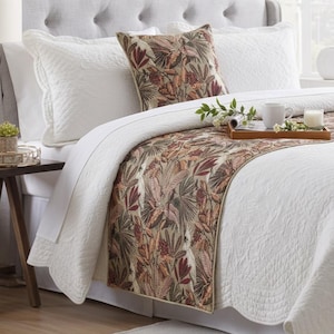May include: A white quilted bedspread and matching pillow shams paired with a decorative runner and square throw pillow featuring a botanical print in shades of rust, brown, and green. The bedding set is arranged on a tufted gray headboard.