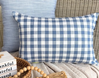 Può includere: Un cuscino rettangolare con motivo a quadretti vichy blu e bianchi, posizionato davanti a un cuscino quadrato azzurro testurizzato. Il cuscino rettangolare presenta una piccola etichetta in tessuto nero sul bordo laterale destro.