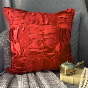 May include: A square throw pillow in a vibrant red color featuring a gathered, ruched fabric texture across the entire surface. The pillow has a structured, pleated design that creates a series of vertical and horizontal channels throughout.