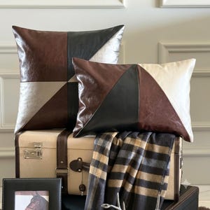 May include: Two decorative throw pillows featuring a geometric color-block design in shades of brown, black, and cream. The square pillow and the rectangular pillow are constructed with smooth panels arranged in triangular patterns.