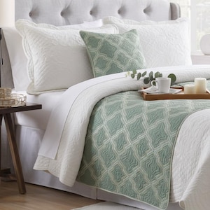 May include: A bedding set featuring a white quilt with a textured pattern, a sage green runner with a geometric lattice design, and a matching square throw pillow. The set includes white pillow shams with scalloped edges and quilted detailing.