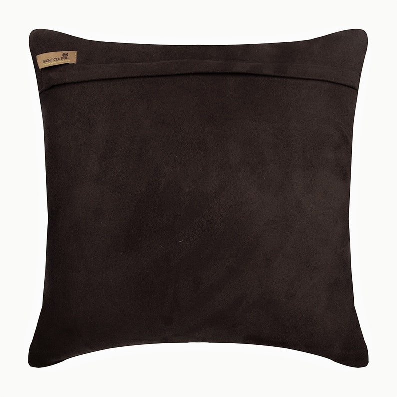 Pode incluir: Uma almofada quadrada marrom escura com uma textura macia semelhante a camur&ccedil;a. A almofada tem um design simples e uma etiqueta que diz "HOME CENTRIC" em uma forma pequena e retangular.