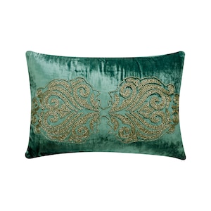 Puede incluir: Una almohada de terciopelo verde azulado con un diseño de cuentas doradas. El diseño es un patrón simétrico de remolinos y curvas.