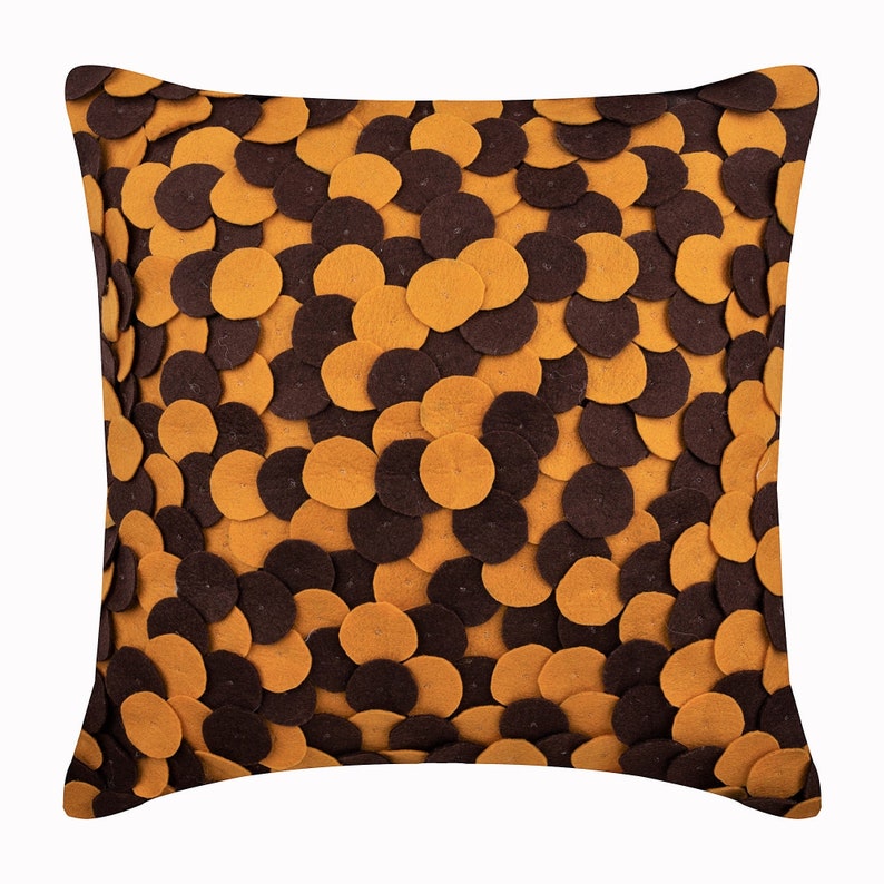 Pode incluir: Almofada decorativa quadrada com um padr&atilde;o de c&iacute;rculos de feltro castanhos e amarelo dourado sobrepostos. A almofada tem um aspeto macio e texturizado, e o design cria um efeito dimensional em camadas. &Eacute; um artigo de decora&ccedil;&atilde;o para casa.