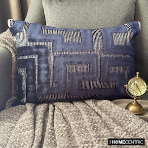 May include: A blue and silver geometric patterned throw pillow on a gray couch with a gold clock on a table in the background.