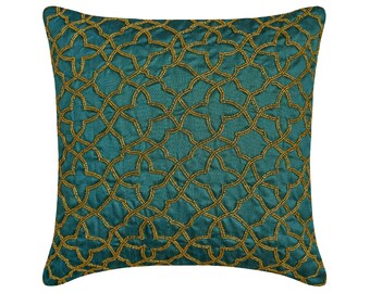 Può includere: Una federa quadrata color verde ottanio profondo caratterizzata da un intricato motivo geometrico a reticolo, realizzato con perline color oro. Il design è composto da forme a stella a quattro punte interconnesse su tutta la superficie.