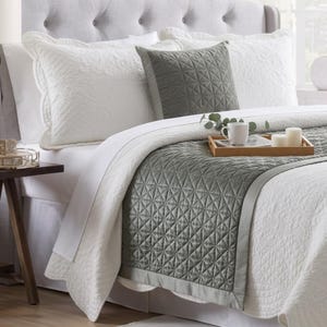 Può includere: Un letto con biancheria trapuntata bianca, un runner trapuntato verde salvia e un cuscino quadrato abbinato. Sul letto è appoggiato un vassoio in legno con una tazza in ceramica bianca e due candele a colonna bianche, decorate da un rametto verde.