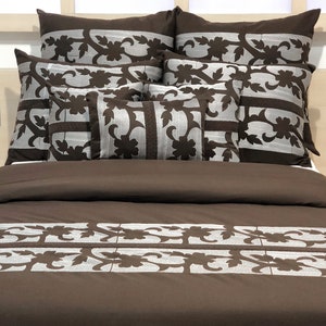 May include: A brown duvet cover with a white floral pattern. The duvet cover is on a bed with several decorative pillows, also featuring a white floral pattern.
