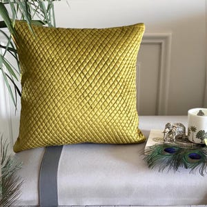 May include: A square throw pillow in a vibrant olive green hue, featuring a quilted diamond pattern across its entire surface. The fabric has a subtle sheen, and the pillow is constructed with clean, straight edges, presenting a uniform texture.