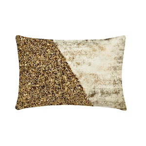 May include: A rectangular throw cushion featuring a diagonal split design. One side is densely covered in shimmering gold sequins and beads, while the other side displays a textured, off-white fabric with subtle, distressed gold metallic accents.