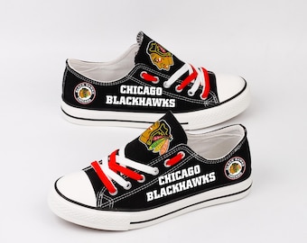Może przedstawiać: Czarne płócienne trampki z białymi podeszwami i czerwonymi i białymi sznurowadłami. Buty posiadają logo i tekst Chicago Blackhawks. Język buta ma logo drużyny. Buty są w stylu niskim.