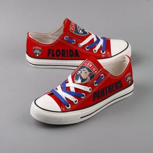 May include: Red canvas low-top sneakers with white laces and a blue accent. The shoes feature a Florida Panthers logo with the team name and "Florida" printed on the side.