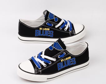 May include: Pair of black canvas sneakers with white soles and toe caps. The shoes feature blue laces and the words "ST. LOUIS BLUES" in blue and white lettering. A blue logo is also visible.