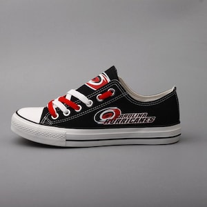 May include: Black canvas low-top sneaker with white toe cap and sole. Features red laces and the Carolina Hurricanes logo in red and white. The team name is printed on the side of the shoe.
