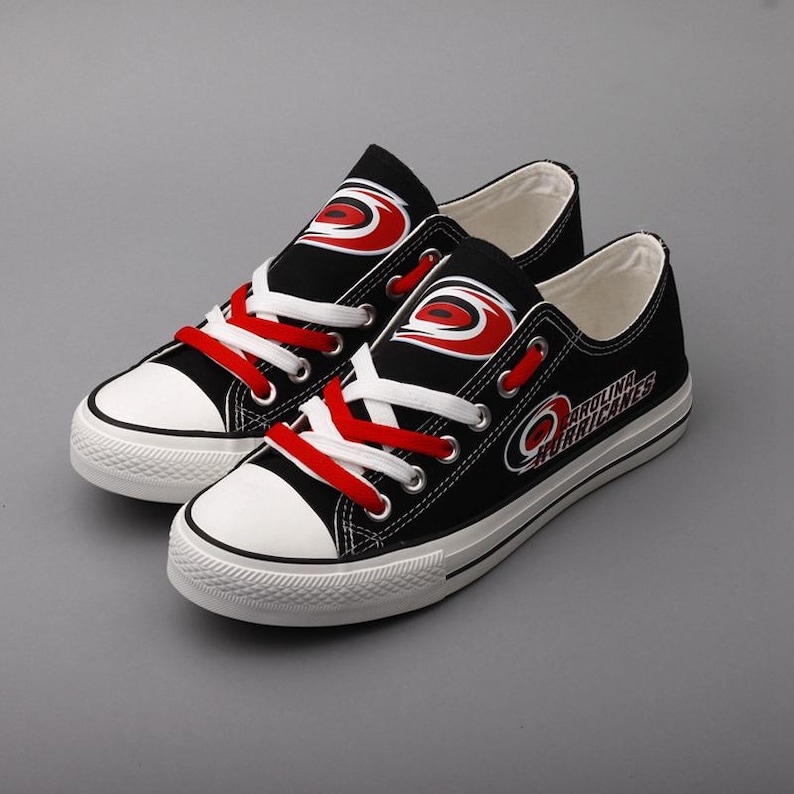 May include: Pair of black canvas sneakers with white soles and toe caps. The sneakers feature red and white laces and the Carolina Hurricanes logo on the sides. The text "CAROLINA HURRICANES" is printed on the side of the shoe.