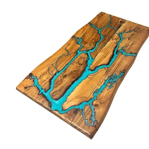 May include: A wooden serving board with a live edge design. The board has a turquoise resin inlay, resembling lightning. The wood has a warm, natural tone, and the resin provides a vibrant contrast. This handcrafted piece is ideal for serving food, measuring approximately 40cm x 20cm.
