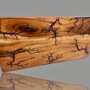 Puede incluir: Una bandeja de madera con un diseño único. La bandeja es de madera marrón claro con patrones púrpuras oscuros en forma de relámpagos. Tiene una forma curva y asas de metal. Aproximadamente 30 cm de largo.