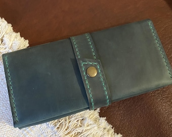 May include: A dark teal leather wallet with a button closure and green stitching. The wallet is rectangular and has a flap that secures with a brass-colored button. The stitching is a contrasting light green color.