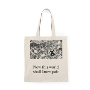 May include: Cream-coloured tote bag with a black and white city map graphic and a figure. The text "Now this world shall know pain" is printed below the graphic. The bag has two long handles.