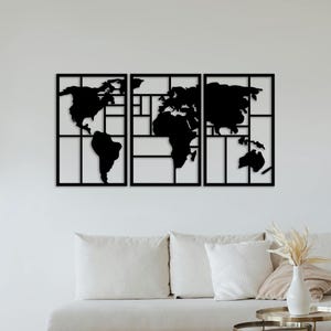 May include: A black metal world map wall decor with a geometric design. The map is divided into three sections, each with a different continent. The map is mounted on a white wall above a white couch with pillows.