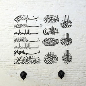 Pode incluir: Uma parede de tijolo branco com caligrafia árabe preta em vários estilos e tamanhos. O texto inclui a frase "Bismillah al-Rahman al-Rahim" que se traduz como "Em nome de Alá, o Mais Misericordioso, o Mais Compassivo".