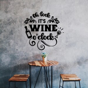 Puede incluir: Decoración de pared en blanco y negro con el texto "Oh look it's wine o'clock" con un gráfico de botella de vino y vaso. La decoración está colgada en una pared de concreto gris sobre una mesa de madera con dos sillas.