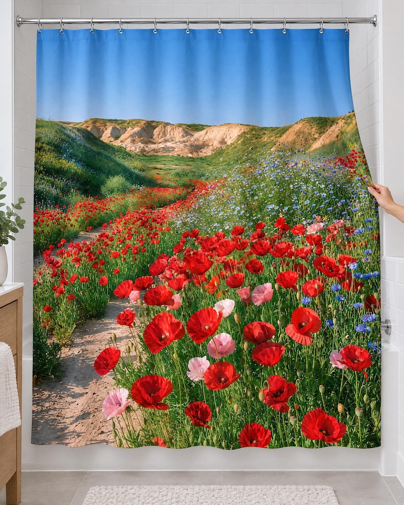 Red poppy wildflower shower curtain over a bathtub in a white-tiled bathroom: red and pink poppies and blue wildflowers line a sandy path toward pale hills under a wide blue sky; a hand pulls back the right edge.