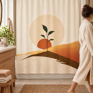 Wider view of a bright bathroom with the boho seedling sun shower curtain closed across the tub, a wooden vanity with a plant and towels to the left and a woman in a cream robe walking past barefoot on a woven rug.