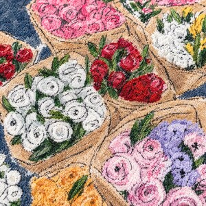 K&ouml;nnte beinhalten: Ein getufteter Teppich mit einem sich wiederholenden Muster aus verschiedenen Blumenstr&auml;u&szlig;en, die in beiges Papier eingewickelt sind. Das Design zeigt Gruppen von rosa, wei&szlig;en, roten, gelben und violetten Bl&uuml;ten mit gr&uuml;nen Bl&auml;ttern auf dunkelblauem Grund.