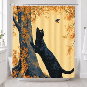 Straight-on view of the whole autumn tree cat shower curtain hanging in a white bathroom, showing the cat reaching up the trunk, a bird in flight, orange leaves and a pale yellow sky.