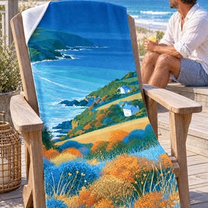 Sea cliff cottage beach towel draped over a wooden Adirondack chair on a seaside deck, a top corner folded back to the white terry back; a man in sunglasses and a white linen shirt sits nearby holding a drink.