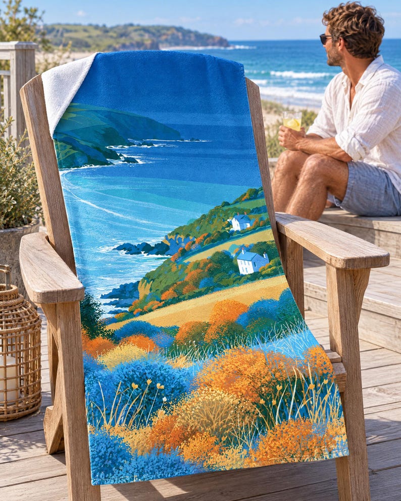 Sea cliff cottage beach towel draped over a wooden Adirondack chair on a seaside deck, a top corner folded back to the white terry back; a man in sunglasses and a white linen shirt sits nearby holding a drink.