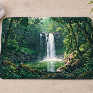 Overhead view of the whole jungle waterfall bath mat on a light wood floor, with rolled white towels, a lit candle and a potted fern beside it.