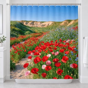 Straight-on view of the whole poppy wildflower shower curtain hanging in a white bathroom, showing the poppy field, blue wildflowers, sandy path, pale eroded hills and clear blue sky.
