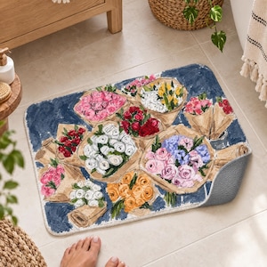 K&ouml;nnte beinhalten: Eine rechteckige Badematte mit dunkelblauem Hintergrund und einem Aquarell-Druck von mehreren Blumenstr&auml;u&szlig;en, die in braunes Papier eingewickelt sind. Die Blumenarrangements zeigen rosa, wei&szlig;e, rote, gelbe, orangefarbene und violette Bl&uuml;ten.