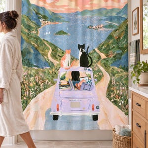 Wider view of a bright bathroom with the lavender car cats shower curtain, its dark-haired driver and two cats, closed across the tub, a woman in a white robe walking past barefoot on the left and a wooden vanity and basket to the right.