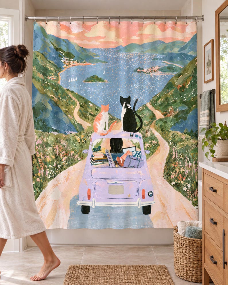 Wider view of a bright bathroom with the lavender car cats shower curtain, its dark-haired driver and two cats, closed across the tub, a woman in a white robe walking past barefoot on the left and a wooden vanity and basket to the right.