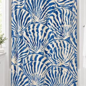 Blue scallop shell shower curtain with overlapping brushy cobalt-blue and cream seashells, hanging on a chrome rod in a white bathroom.