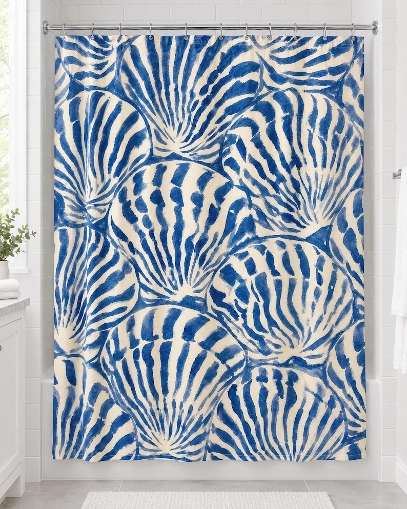 Blue scallop shell shower curtain with overlapping brushy cobalt-blue and cream seashells, hanging on a chrome rod in a white bathroom.