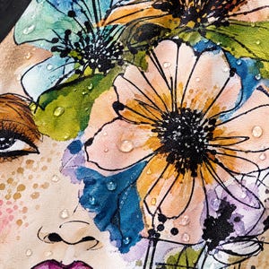 May include: A fabric print featuring a stylized face adorned with large, vibrant watercolor flowers in shades of orange, blue, green, and purple. The design includes black ink outlines, scattered gold-toned speckles, and clear water droplets.