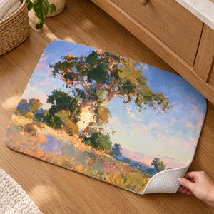 May include: A rectangular floor mat featuring an impressionistic landscape painting of a large tree standing in a grassy field under a bright blue sky. The artwork uses visible brushstrokes in shades of green, yellow, orange, and blue.