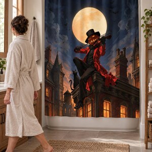 Wider view of a bright bathroom with the pumpkin violinist shower curtain closed across the tub, showing gothic brick towers and glowing windows under a full moon; a woman in a robe walks past barefoot.