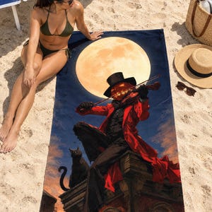 Halloween pumpkin violinist beach towel laid on sand, printed with a pumpkin-headed figure in a red coat and top hat playing a violin before a full moon, as a woman in a bikini sits beside it.