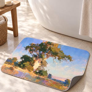 May include: A rectangular bath mat featuring an impressionistic landscape painting of a large tree with green foliage set against a light blue sky. The ground is depicted with textured brushstrokes in shades of yellow, orange, and purple.