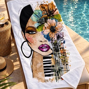 May include: A white beach towel featuring a colorful watercolor-style illustration of a face with vibrant purple lips, large hoop earrings, and a head of flowers. The design includes black and white piano keys and abstract paint splatters.