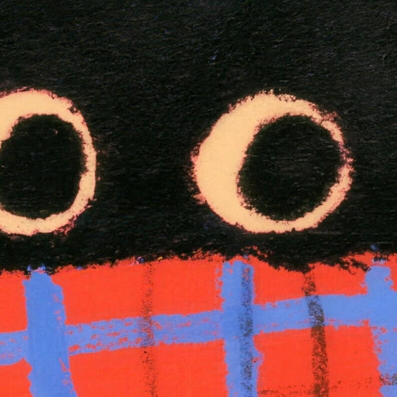 Close-up of the bath mat's print: the cat's two round cream-ringed eyes above a red-orange plaid scarf with blue stripes.